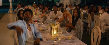 Movie still from “Do Revenge” (2022), directed by Jennifer Kaytin Robinson – A group of people sitting at a table with candles; Medium shot, Over the shoulder angle
