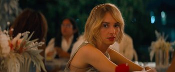 Movie still from “Do Revenge” (2022), directed by Jennifer Kaytin Robinson – A beautiful young lady sitting in front of a group of people; Close Up shot, Over the shoulder angle