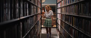 Movie still from “Do Revenge” (2022), directed by Jennifer Kaytin Robinson – A woman in a library looking at books on a shelf; Medium shot, Low angle