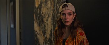 Movie still from “Do Revenge” (2022), directed by Jennifer Kaytin Robinson – A woman wearing a hat standing in front of a painting; Close Up shot, Over the shoulder angle