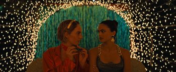 Movie still from “Do Revenge” (2022), directed by Jennifer Kaytin Robinson – Two women standing next to each other in front of lights; Close Up shot, Over the shoulder angle