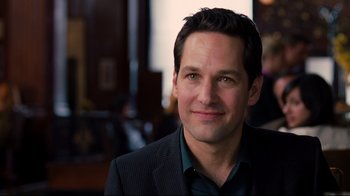 Movie still from “Dinner for Schmucks” (2010), directed by Jay Roach – A man that is wearing a suit and smiling; Close Up shot, Over the shoulder angle