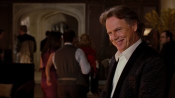 Movie still from “Dinner for Schmucks” (2010), directed by Jay Roach – A man in a suit and tie standing in front of a group of people; Close Up shot, Over the shoulder angle