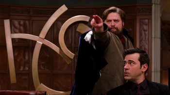 Movie still from “Dinner for Schmucks” (2010), directed by Jay Roach – A man standing next to another man in front of a wall; Medium shot, Over the shoulder angle