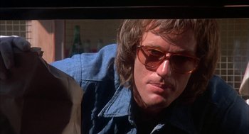 Movie still from “Dirty Mary Crazy Larry” (1974), directed by John Hough – A man wearing a jean jacket and sunglasses; Close Up shot, Low angle