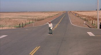 Movie still from “Dirty Mary Crazy Larry” (1974), directed by John Hough – A man riding a skateboard down the middle of a road; Extreme Wide shot, High angle