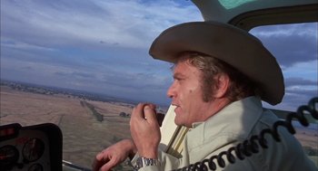 Movie still from “Dirty Mary Crazy Larry” (1974), directed by John Hough – A man wearing a cowboy hat while sitting in a helicopter; Medium shot, Low angle
