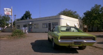 Movie still from “Dirty Mary Crazy Larry” (1974), directed by John Hough – A car parked in front of a building on the side of the road; Wide shot, Low angle
