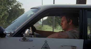 Movie still from “Dirty Mary Crazy Larry” (1974), directed by John Hough – A man sitting in the driver's seat of a car; Medium shot, Low angle