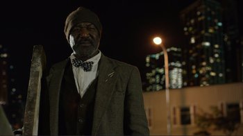 Movie still from “Do You Believe?” (2015), directed by Jon Gunn – A man wearing a suit and bow tie standing in front of a street light; Medium shot, Low angle
