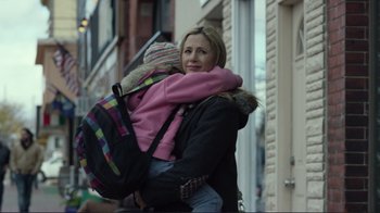 Movie still from “Do You Believe?” (2015), directed by Jon Gunn – A woman carrying a child on her back while walking down the street; Close Up shot, Over the shoulder angle