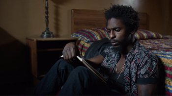 Movie still from “Do You Believe?” (2015), directed by Jon Gunn – A man sitting on a bed with a book in his hand; Close Up shot, Low angle
