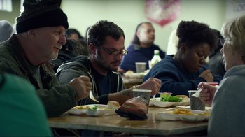 Movie still from “Do You Believe?” (2015), directed by Jon Gunn – A group of people sitting at a table eating food; Medium shot, Over the shoulder angle