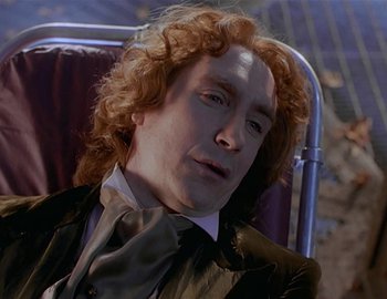 Movie still from “Doctor Who: The Movie” (1996), directed by Geoffrey Sax – A man with red hair sitting in a chair wearing a suit and tie; Close Up shot, High angle