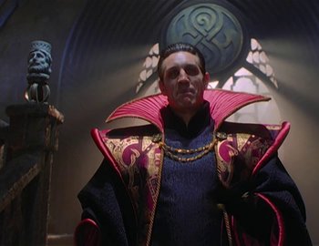 Movie still from “Doctor Who: The Movie” (1996), directed by Geoffrey Sax – A man in a red and black outfit standing next to a statue; Medium shot, Low angle