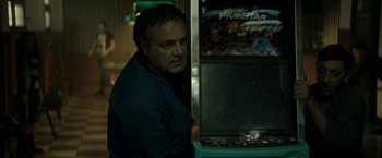 Movie still from “Dogman” (2018), directed by Matteo Garrone – A man standing next to a video game machine; Medium shot, Over the shoulder angle