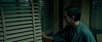 Movie still from “Dogman” (2018), directed by Matteo Garrone – A man looking out of a window blinds; Medium shot, Low angle