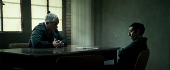 Movie still from “Dogman” (2018), directed by Matteo Garrone – An older man sitting at a table in front of a window; Medium shot, Over the shoulder angle