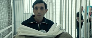 Movie still from “Dogman” (2018), directed by Matteo Garrone – A man sitting in front of a stack of newspapers; Close Up shot, Low angle