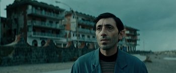 Movie still from “Dogman” (2018), directed by Matteo Garrone – A man standing in front of a tall building; Close Up shot, Low angle
