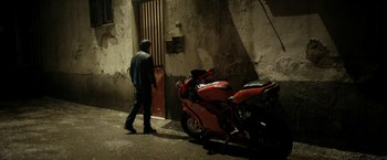 Movie still from “Dogman” (2018), directed by Matteo Garrone – A man standing next to a red motorcycle; Wide shot, High angle