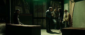 Movie still from “Dogman” (2018), directed by Matteo Garrone – A group of people standing around in a room; Wide shot, Over the shoulder angle