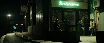 Movie still from “Dogman” (2018), directed by Matteo Garrone – A person sitting on a ledge in front of a building; Wide shot, Low angle