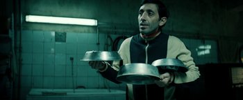 Movie still from “Dogman” (2018), directed by Matteo Garrone – A man holding three metal pans in his hands; Medium shot, Low angle