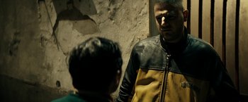 Movie still from “Dogman” (2018), directed by Matteo Garrone – A man in a yellow and black jacket talking to another man; Medium shot, Over the shoulder angle
