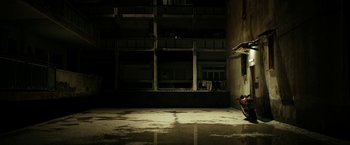 Movie still from “Dogman” (2018), directed by Matteo Garrone – A person sitting in a dark room next to a building; Extreme Wide shot, Low angle