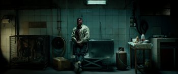 Movie still from “Dogman” (2018), directed by Matteo Garrone – A man sitting on a chair in a room; Wide shot, High angle