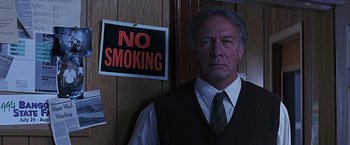 Movie still from “Dolores Claiborne” (1995), directed by Taylor Hackford – An older man wearing a vest and a tie standing in front of a no smoking sign; Close Up shot, Low angle