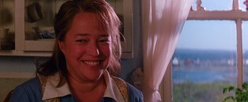Movie still from “Dolores Claiborne” (1995), directed by Taylor Hackford – A woman smiling for the camera in front of a window; Close Up shot, Over the shoulder angle