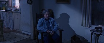 Movie still from “Dolores Claiborne” (1995), directed by Taylor Hackford – An older woman sitting in a rocking chair in a dark room; Medium shot, High angle