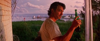 Movie still from “Dolores Claiborne” (1995), directed by Taylor Hackford – A man in a white t - shirt is looking at the water; Medium shot, Low angle
