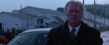 Movie still from “Dolores Claiborne” (1995), directed by Taylor Hackford – An older man wearing a suit and tie standing in front of a car; Close Up shot, Low angle
