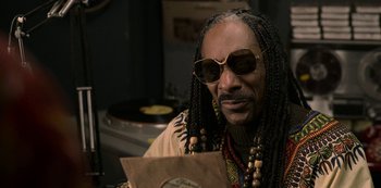 Movie still from “Dolemite Is My Name” (2019), directed by Craig Brewer – A man with long dreadlocks wearing sunglasses and holding a record; Close Up shot, Over the shoulder angle