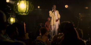 Movie still from “Dolemite Is My Name” (2019), directed by Craig Brewer – A man in a yellow jacket singing into a microphone on a stage; Wide shot, Over the shoulder angle