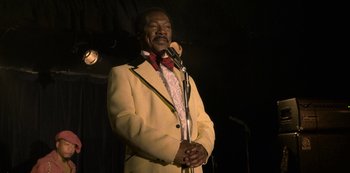 Movie still from “Dolemite Is My Name” (2019), directed by Craig Brewer – A man in a yellow suit is holding a microphone; Medium shot, Low angle