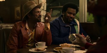 Movie still from “Dolemite Is My Name” (2019), directed by Craig Brewer – A couple of men sitting at a table with food; Medium shot, Over the shoulder angle