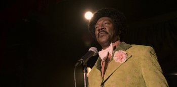 Movie still from “Dolemite Is My Name” (2019), directed by Craig Brewer – A man in a green suit is on a microphone; Close Up shot, Over the shoulder angle