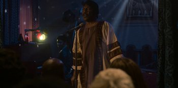 Movie still from “Dolemite Is My Name” (2019), directed by Craig Brewer – A man in a colorful outfit is speaking into a microphone; Medium shot, Over the shoulder angle