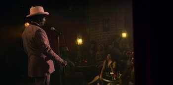 Movie still from “Dolemite Is My Name” (2019), directed by Craig Brewer – A man standing on a stage with a microphone in front of a crowd of onlookers; Wide shot, Over the shoulder angle