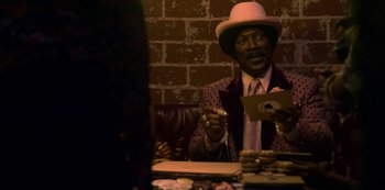 Movie still from “Dolemite Is My Name” (2019), directed by Craig Brewer – A man sitting at a table in front of a brick wall; Medium shot, Over the shoulder angle