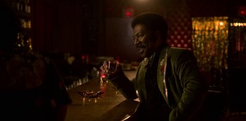 Movie still from “Dolemite Is My Name” (2019), directed by Craig Brewer – A man sitting at a bar holding a glass of wine; Medium shot, Over the shoulder angle