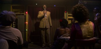 Movie still from “Dolemite Is My Name” (2019), directed by Craig Brewer – A man in a brown suit is holding a microphone; Wide shot, Over the shoulder angle