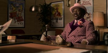 Movie still from “Dolemite Is My Name” (2019), directed by Craig Brewer – A man sitting at a table in a room; Medium shot, Low angle