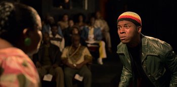 Movie still from “Dolemite Is My Name” (2019), directed by Craig Brewer – A man in a crowd of people sitting in front of a wall; Medium shot, Over the shoulder angle