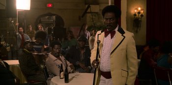 Movie still from “Dolemite Is My Name” (2019), directed by Craig Brewer – A man standing in front of a table with a microphone; Medium shot, Over the shoulder angle