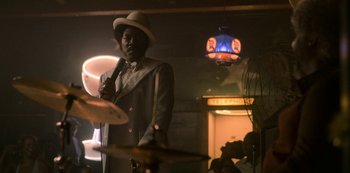 Movie still from “Dolemite Is My Name” (2019), directed by Craig Brewer – A man wearing a hat and holding a microphone in front of drums; Medium shot, Over the shoulder angle